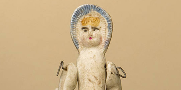 This small molded doll with painted facial features is made of bisque. She has blond hair and movable arms.